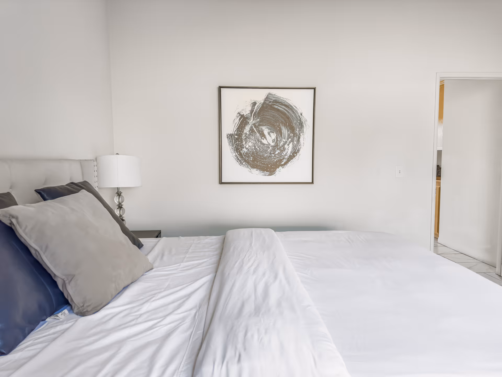 A neatly made bedroom featuring a large bed, decorative pillows, wall art, and a doorway.