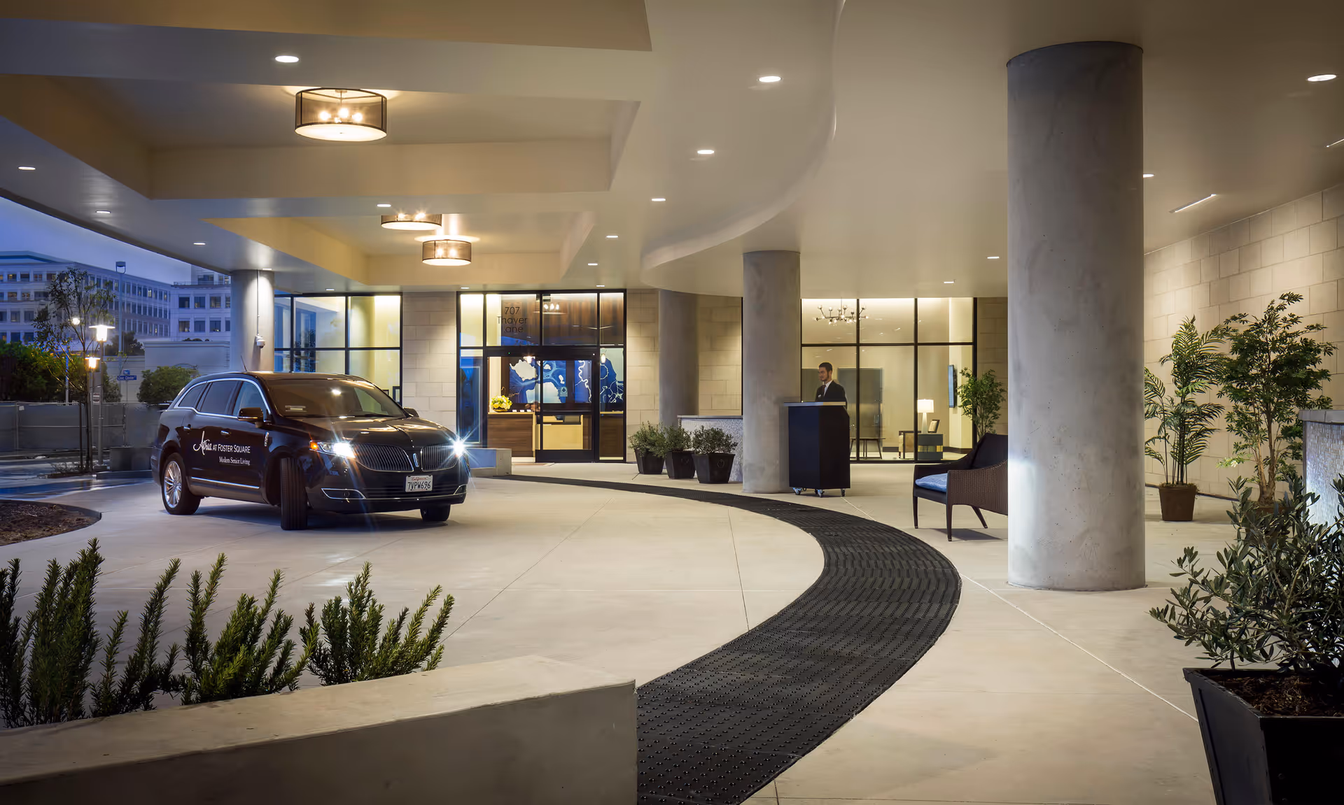 Covered driveway entrance to Atria at Foster Square with car, glass doors, and reception podium.
