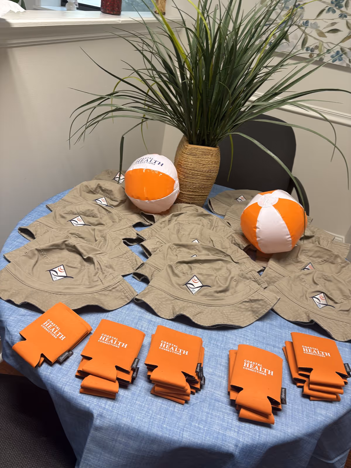 Indoor display table featuring tan shirts and orange Coastal Health promos beside a plant.