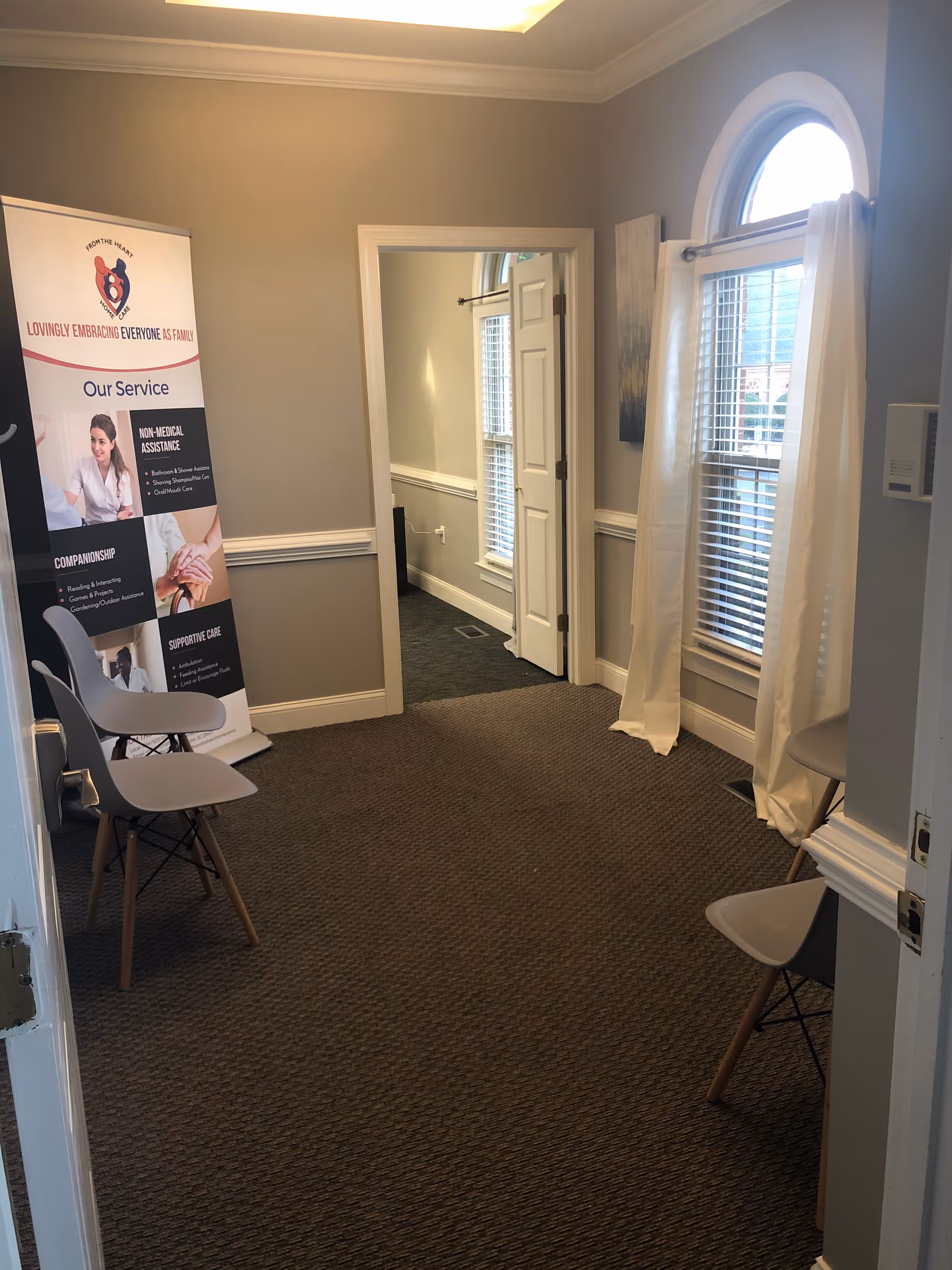 Interior hallway of From The Heart Home Care with chairs, banner, and arched window.