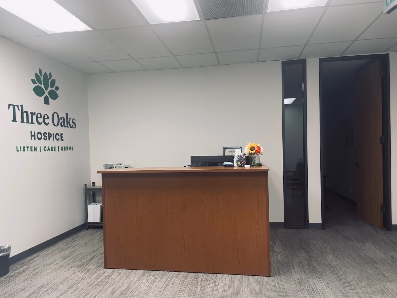 Reception desk in a Three Oaks Hospice lobby with logo on the wall.