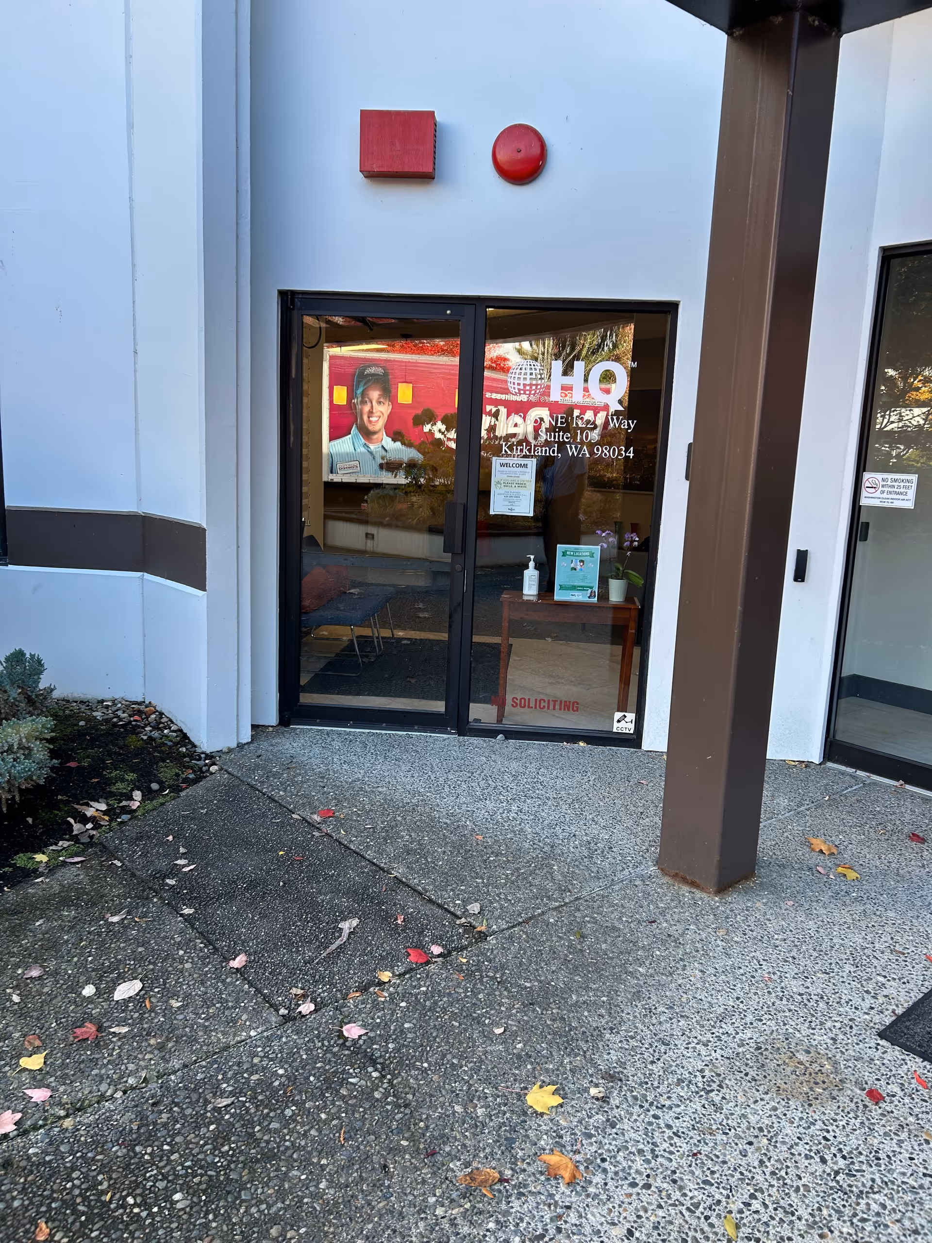 Exterior building entrance with glass doors, red wall fixtures, and scattered autumn leaves.