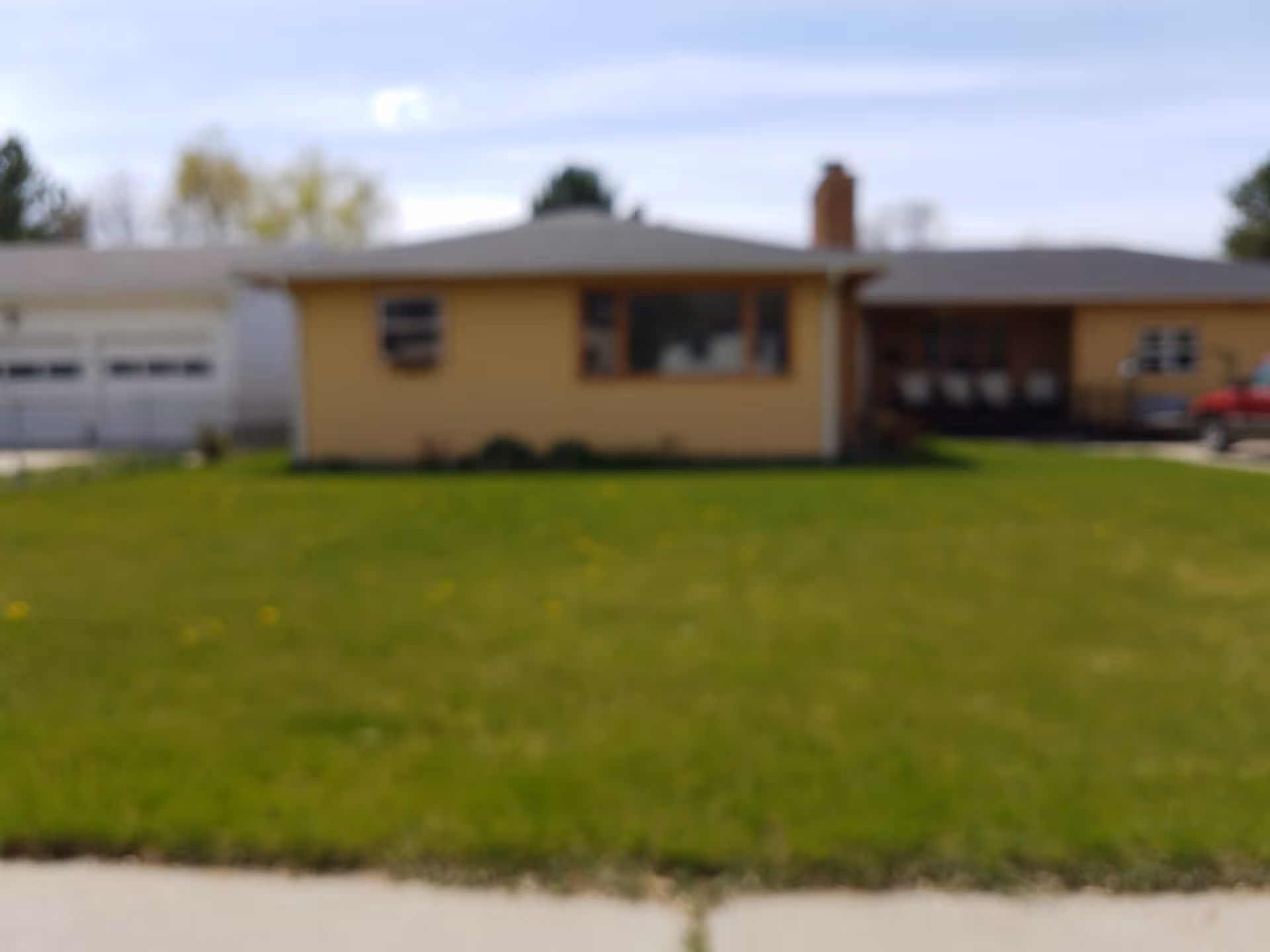 Blurry single-story yellow building with green lawn and driveway in front.
