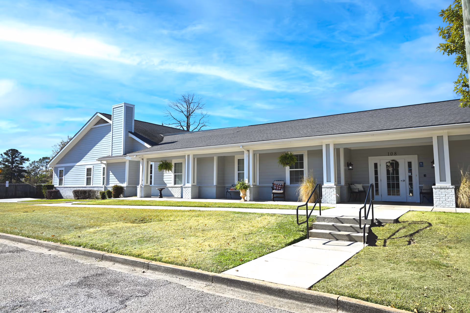 Single-story memory care facility with a wide front porch, steps, and manicured lawn.