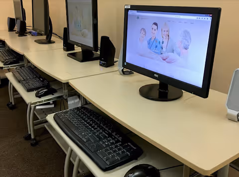 Row of computer desks with monitors, keyboards, and mice in a senior living facility computer room.