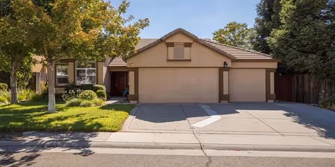 Single-story suburban building front with driveway, two garage doors, and a manicured lawn.