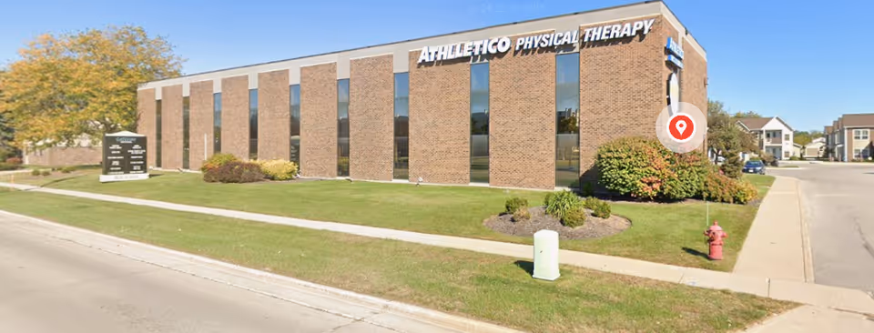 Exterior view of a brick Athletico Physical Therapy building with large windows and landscaping.