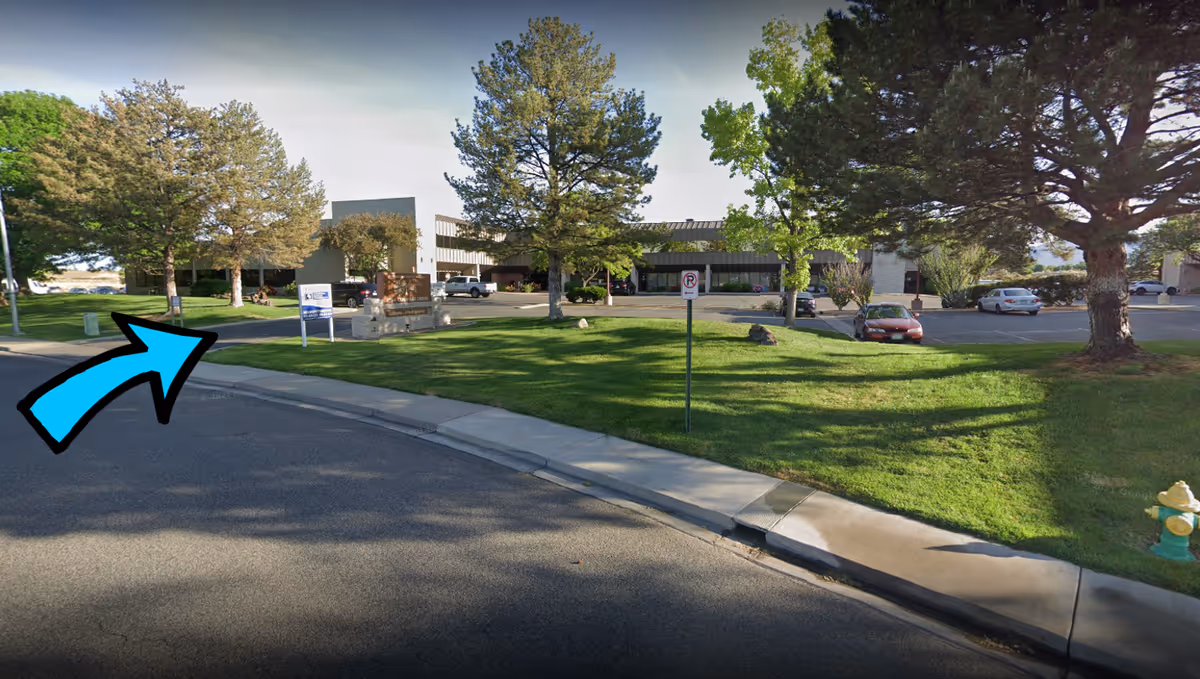 Exterior view of a senior care facility with green lawn, trees, and a parking lot