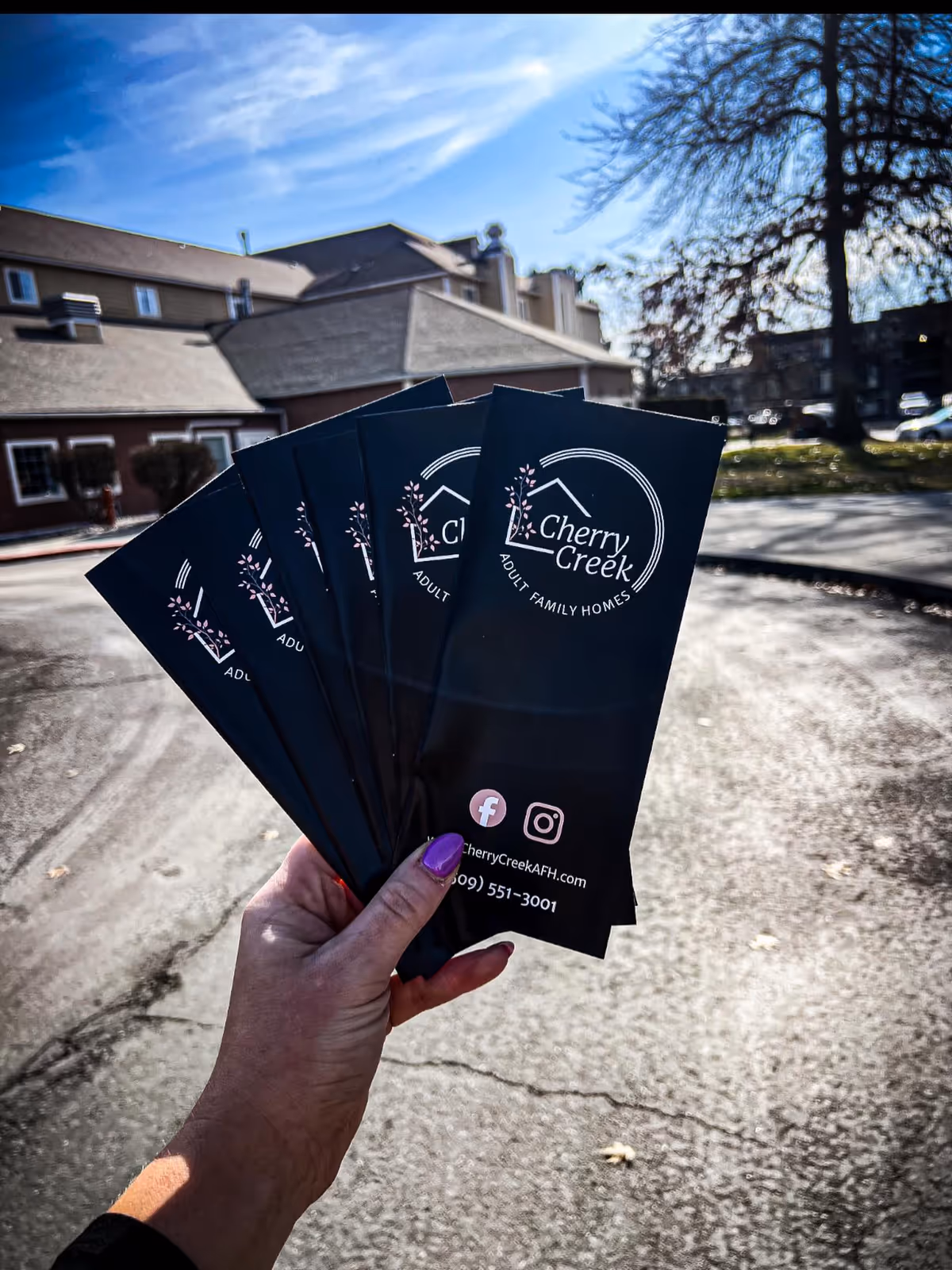 A hand holds Cherry Creek Adult Family Home brochures in front of the facility exterior.