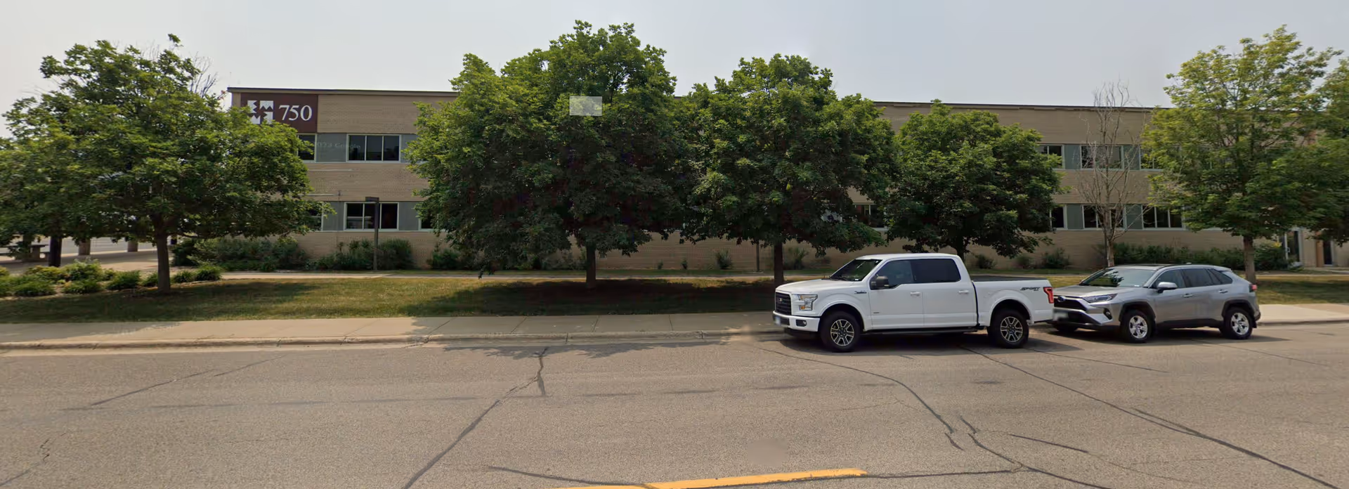 Exterior view of a senior care facility with trees and parked cars along the street