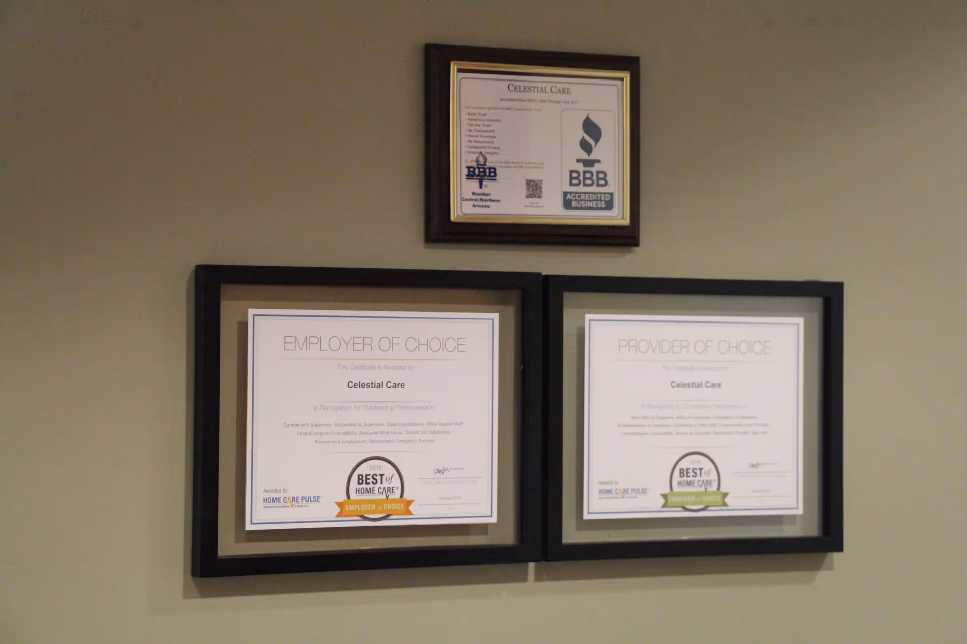 Three framed certificates hang on a beige wall, two large frames side by side.