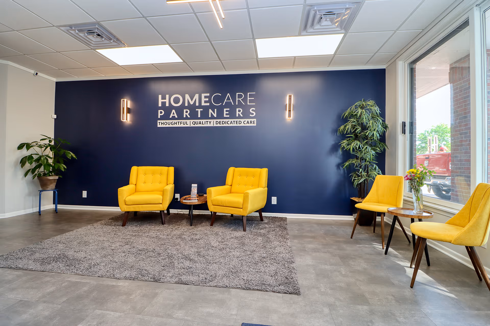 Lobby seating area with blue accent wall, yellow chairs, plants, and a HomeCare Partners sign.
