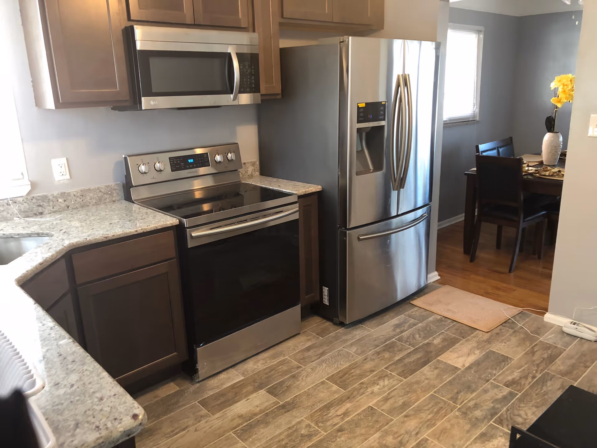 Modern kitchen with granite countertops, stainless steel stove, microwave, and refrigerator opening to a small dining area.
