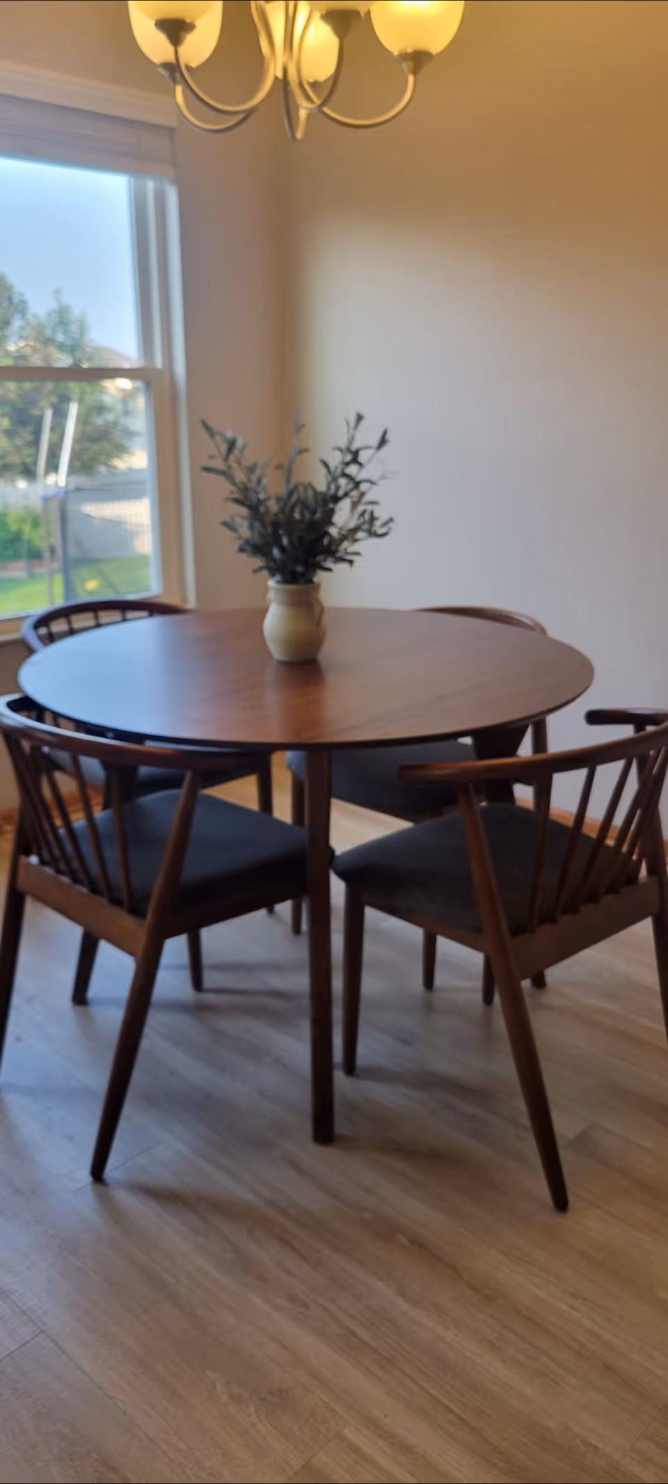 Interior dining room with a round table, chairs, chandelier, and vase centerpiece.