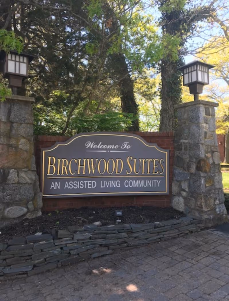 Stone entrance sign reads Birchwood Suites, welcoming visitors to an assisted living community.