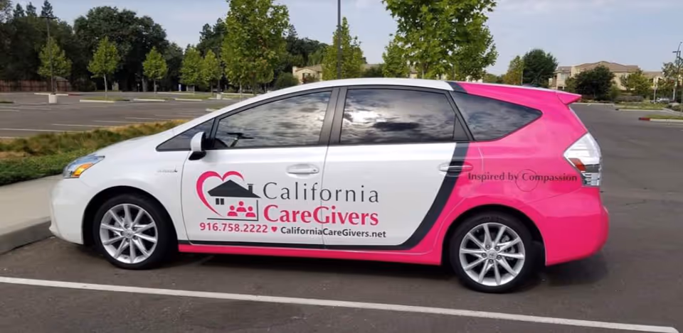 A pink and white California CareGivers promotional car parked in a lot.