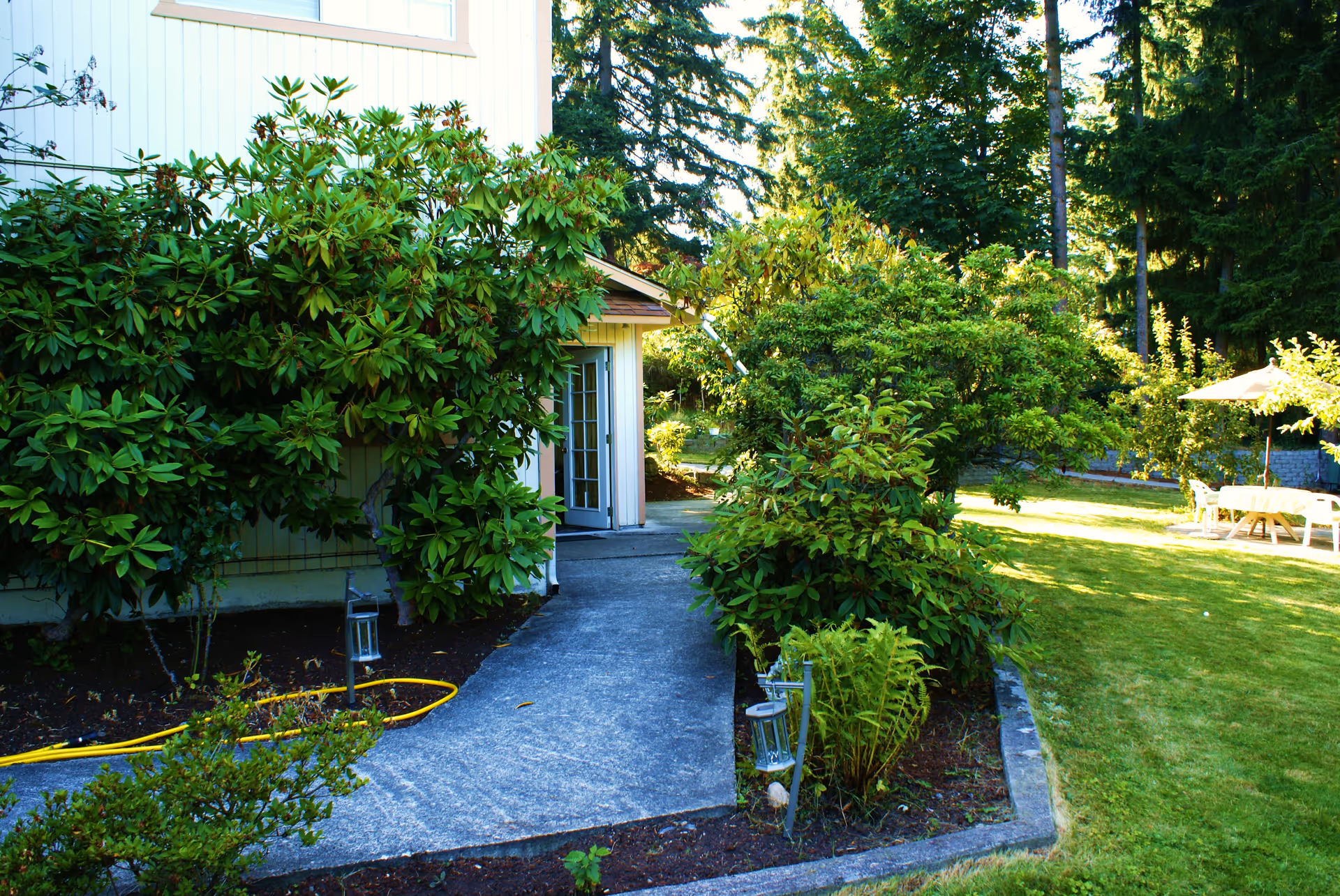 Entrance pathway with shrubs and a sunny outdoor seating area.