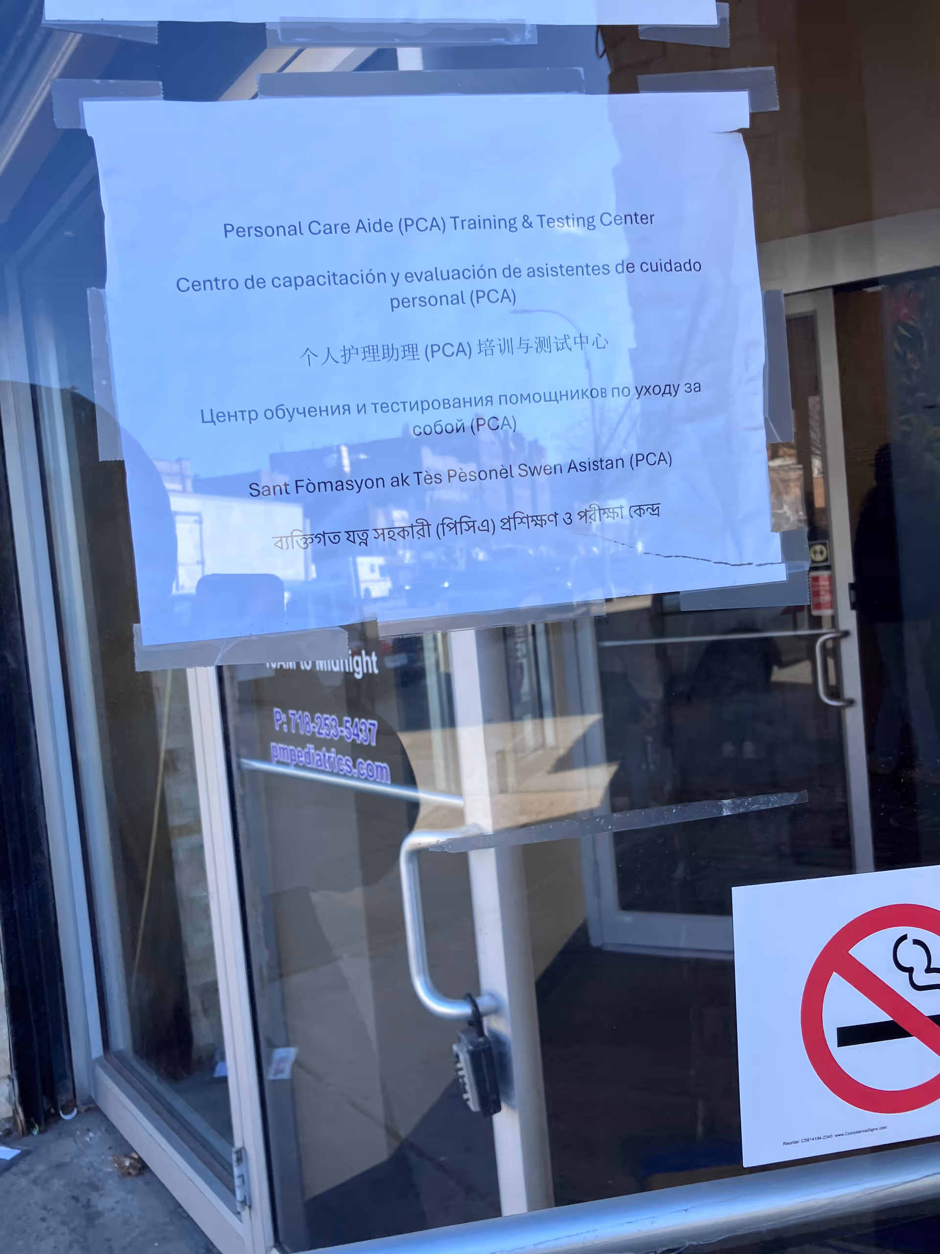 Glass front entrance with a taped multilingual notice on the door of a senior care facility.