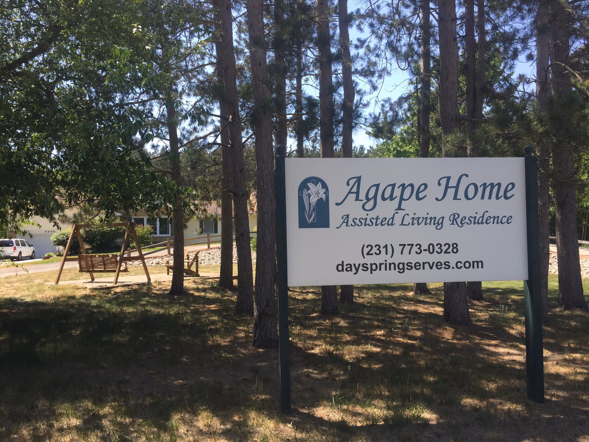 A freestanding sign for Agape Home Assisted Living Residence in front of pine trees and a house.