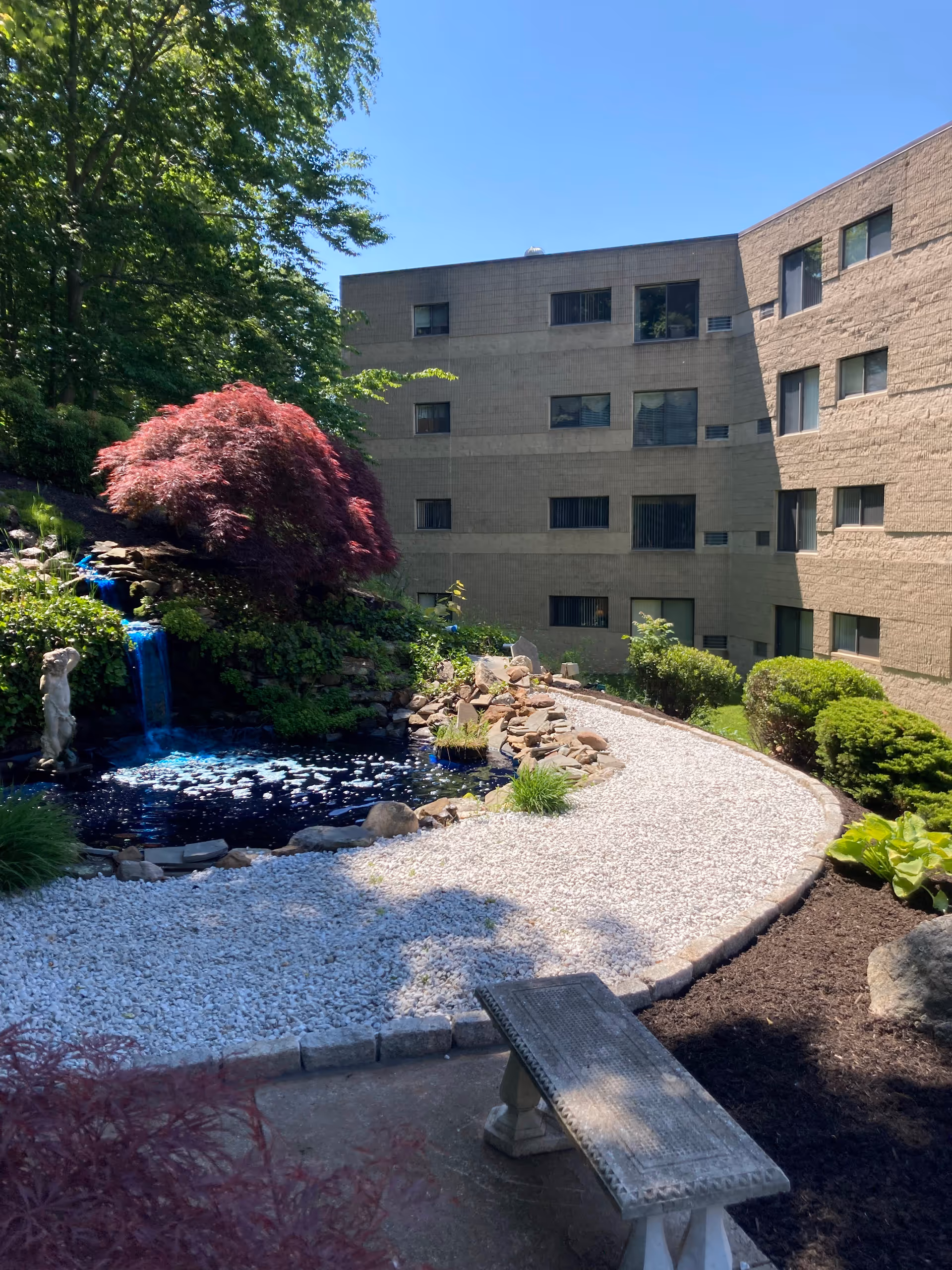 Outdoor courtyard at Woodview Elderly Housing with a pond, rocks, and a stone bench.