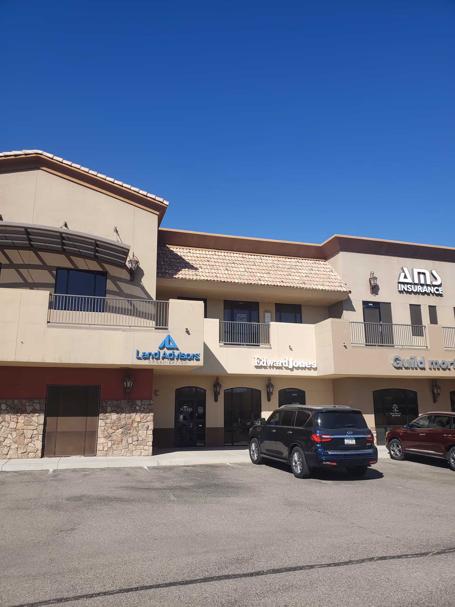 Exterior view of a beige commercial building with storefronts and parked cars.