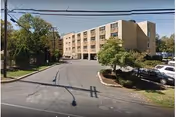 Exterior view of Nyack Ridge Rehabilitation & Nursing Center with driveway, trees, and parked cars.