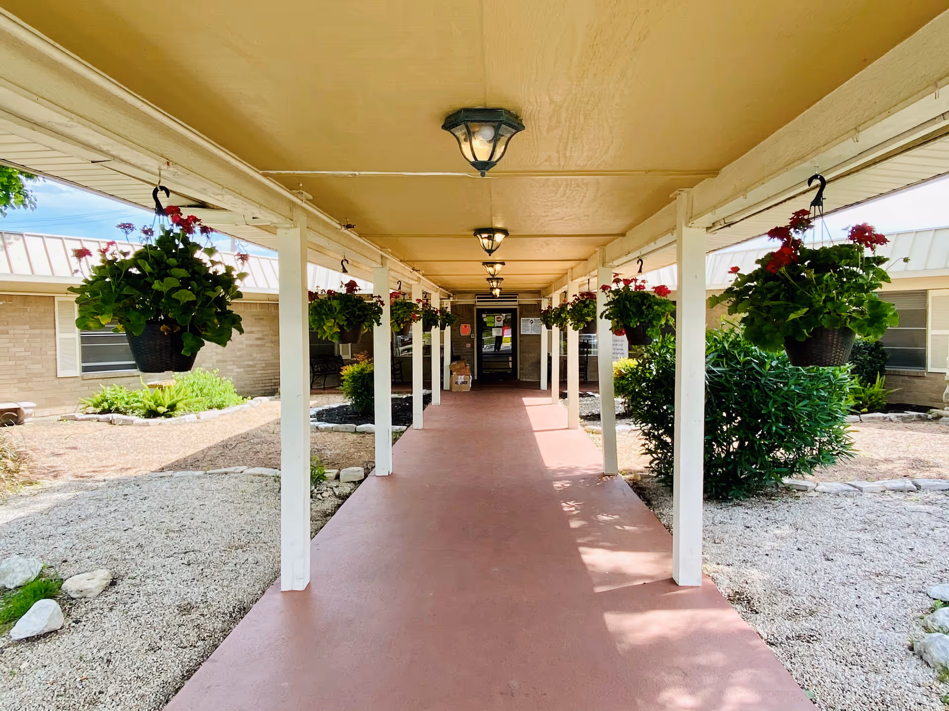 Covered outdoor walkway lined with hanging flower baskets leading to a building entrance