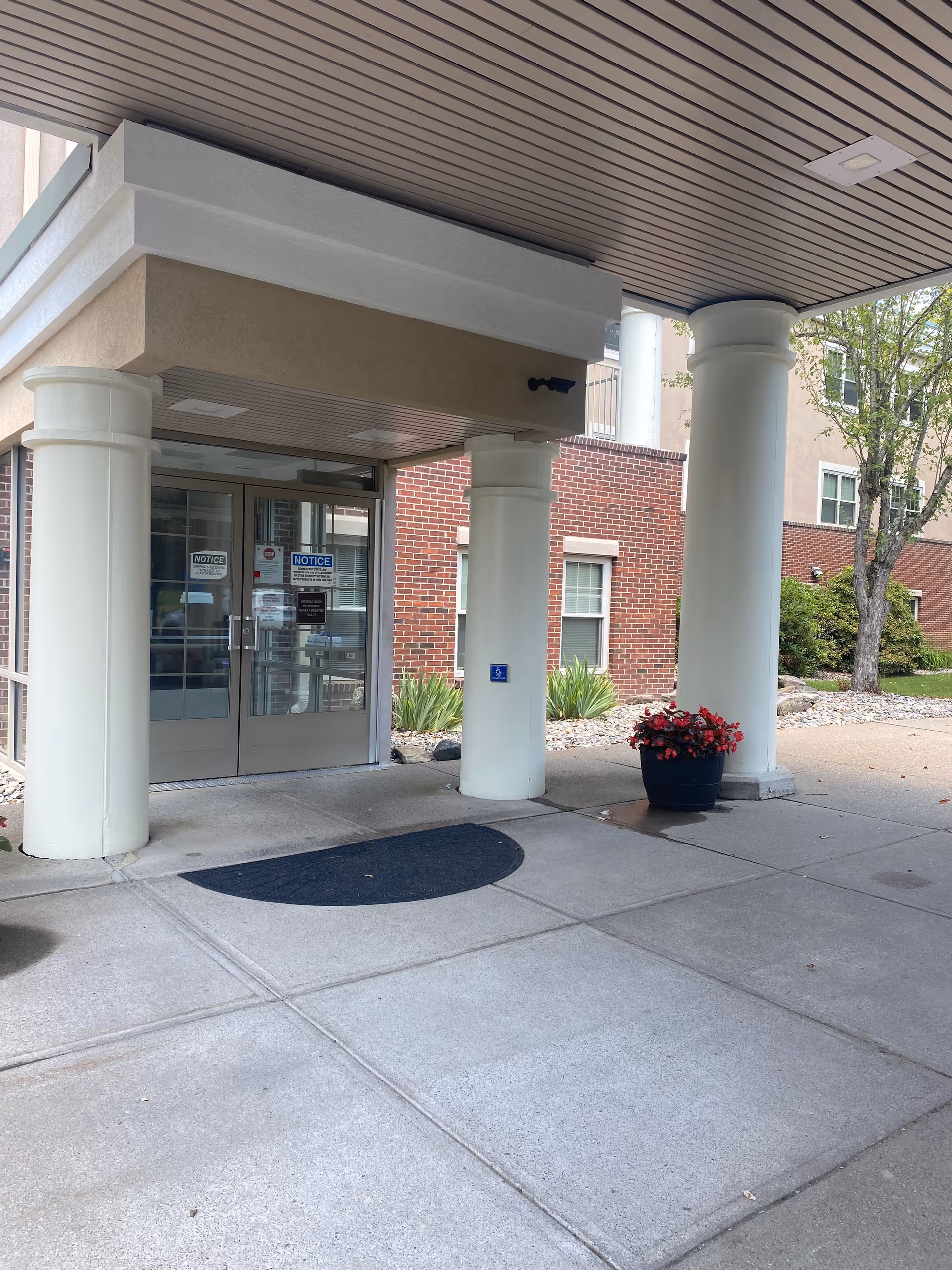 Entrance to a nursing facility with glass doors, white columns, and a planter.