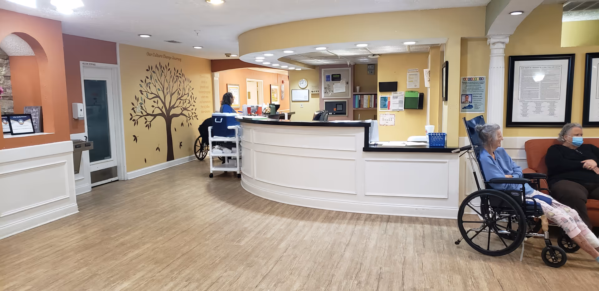 Reception area of Hermitage Care and Rehabilitation Center with a curved desk, residents, and staff.