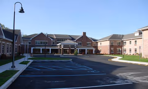 Exterior view of a brick senior living campus with parking lot and curved driveway.