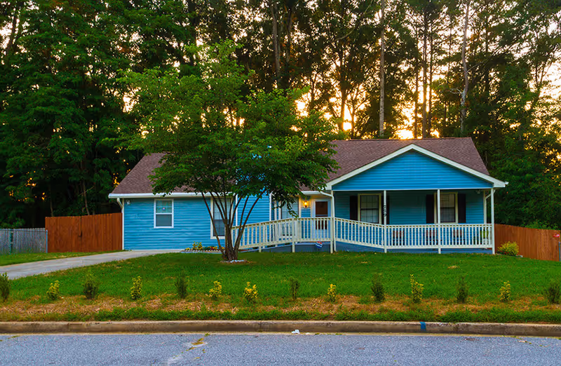 Blue single-story house with a white porch and green lawn.