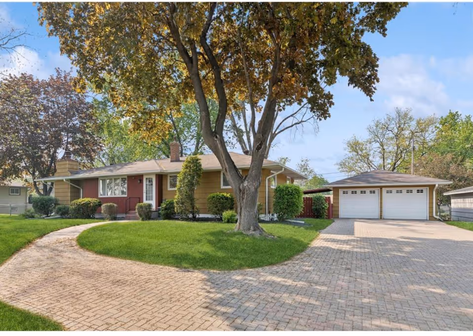 A single-story facility exterior with a curved brick driveway and a large tree in front.