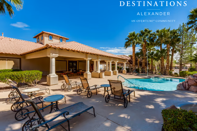 Outdoor pool area at Destinations Alexander featuring lounge chairs, tables, palm trees, and a covered patio with columns under a clear blue sky.