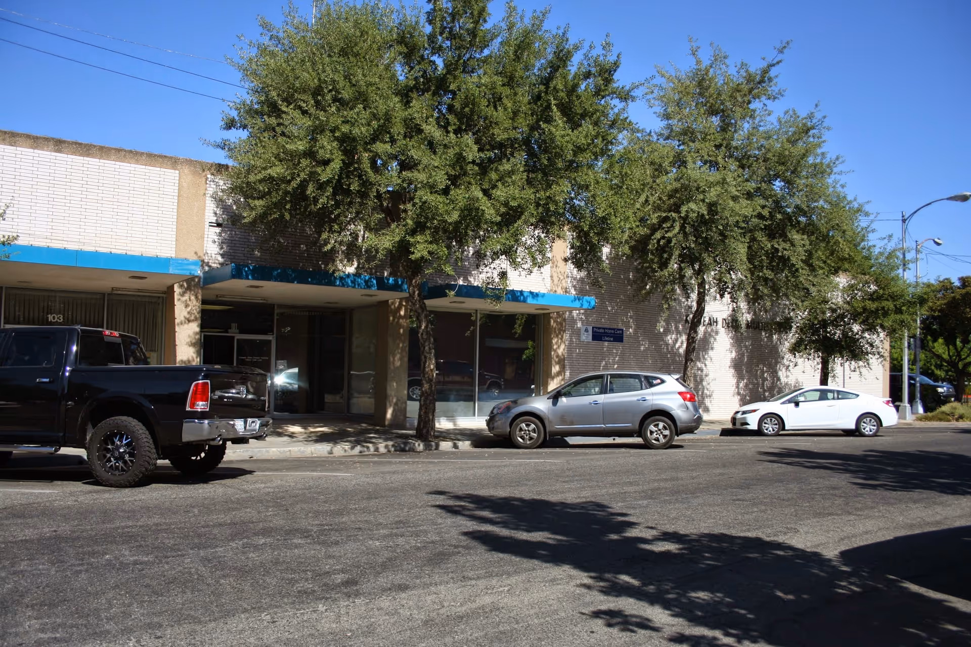 Exterior view of a single-story building with blue awnings and parked cars.
