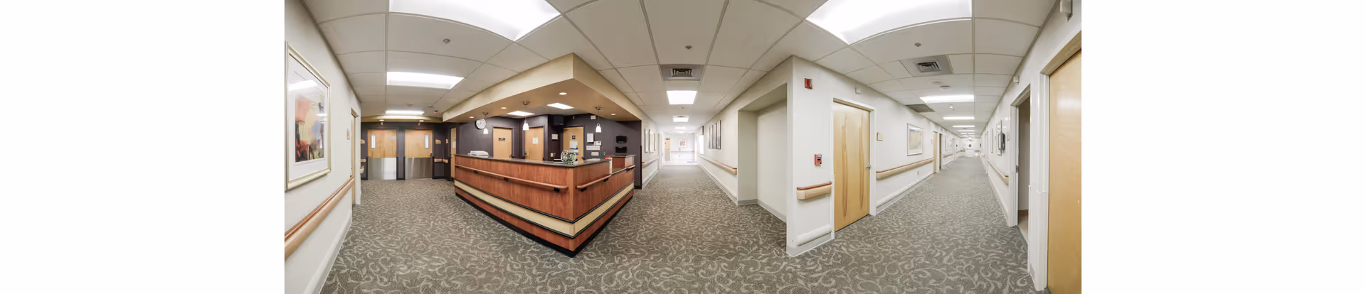 Long hallway in a senior living facility with a central reception desk and doors along sides.