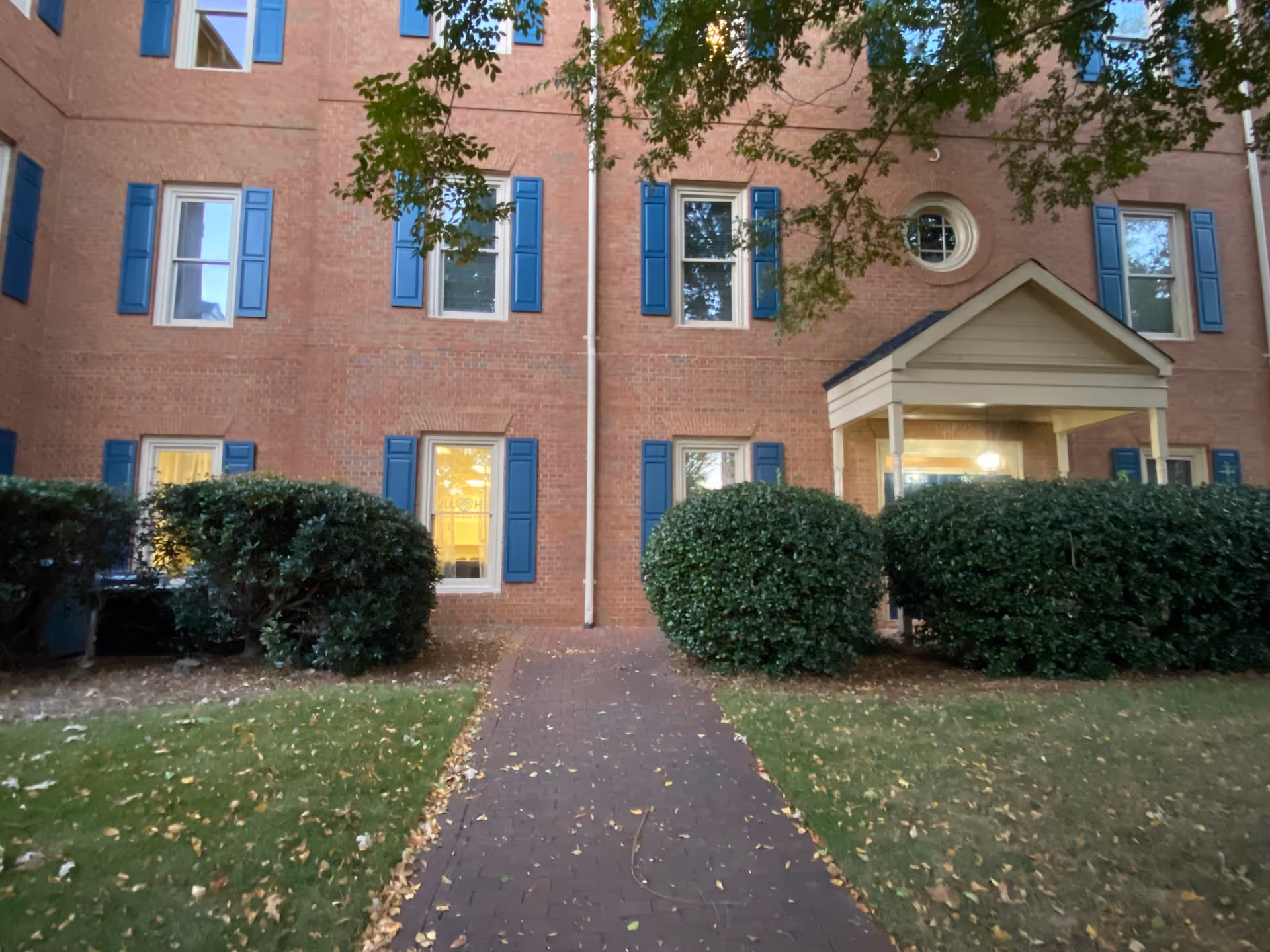 Brick building with blue shutters, front entry porch, and trimmed hedges.