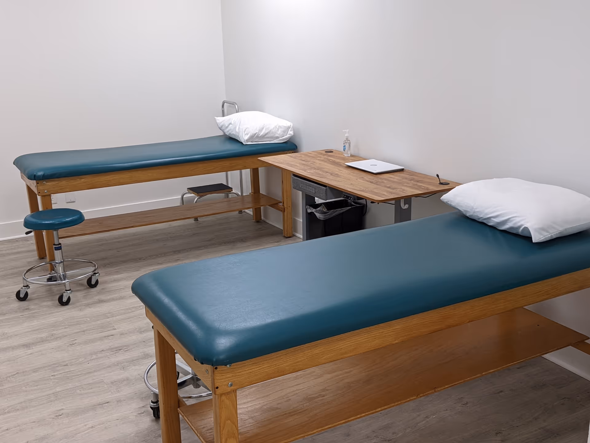 Two teal therapy tables in a clinical treatment room with a desk and laptop.