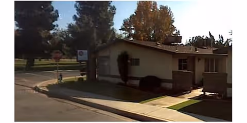 Small single-story beige building with a lawn and trees nearby.