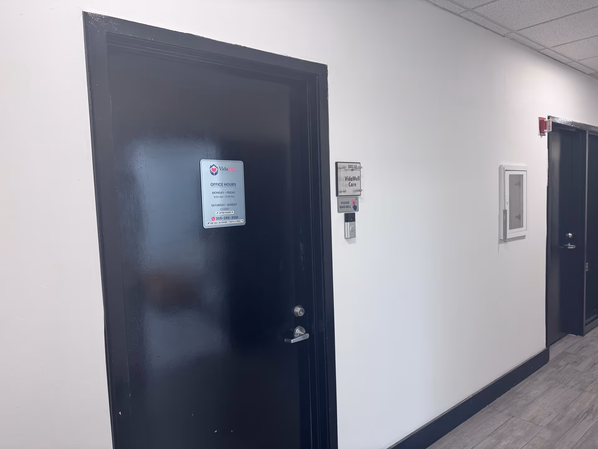 A hallway inside a VidaWell Care facility with black doors and signs.