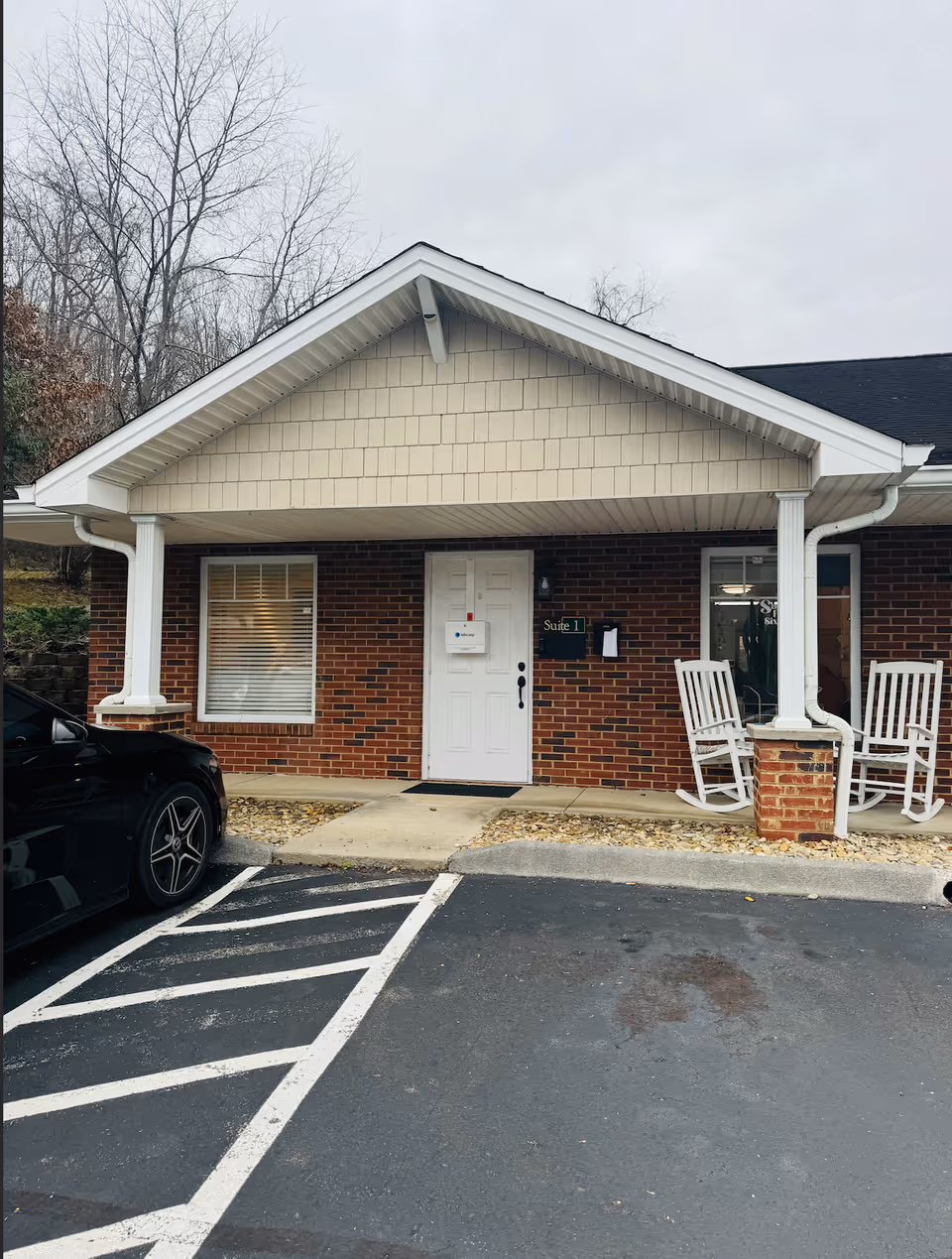Brick senior living facility exterior with white door, porch columns, and rocking chairs.