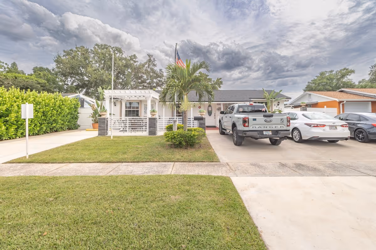 Front exterior of Mis Abuelos Home Care Corp facility, with driveway, vehicles, and palm trees.