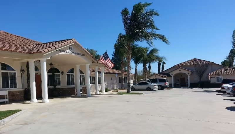 Exterior view of The Gardens of Riverside with columns, palm trees, and cars.
