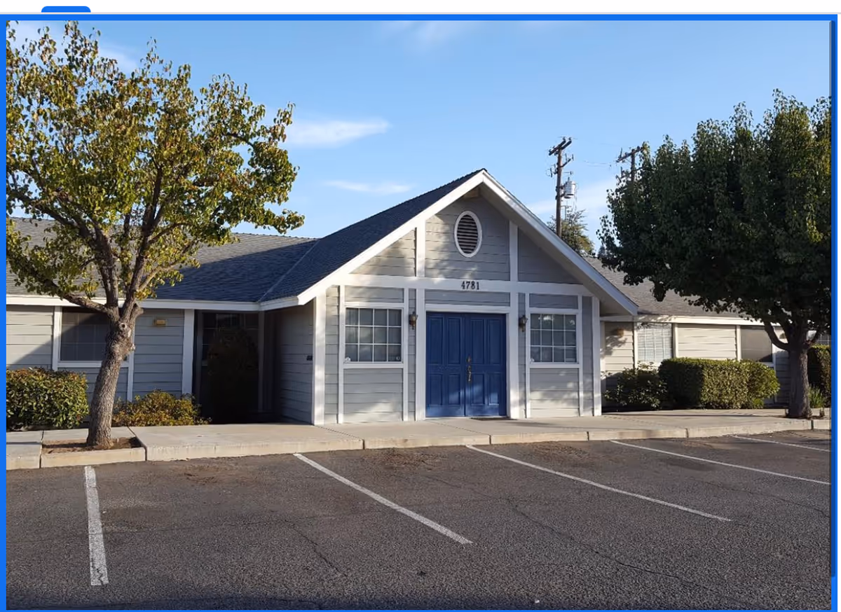 Front view of a single-story facility with blue double doors, trees, and a parking lot.