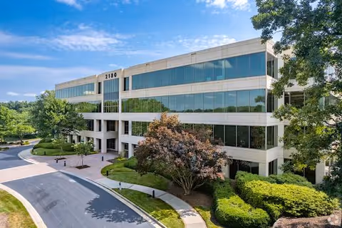 Modern glass-front building with landscaped grounds and a curved driveway.