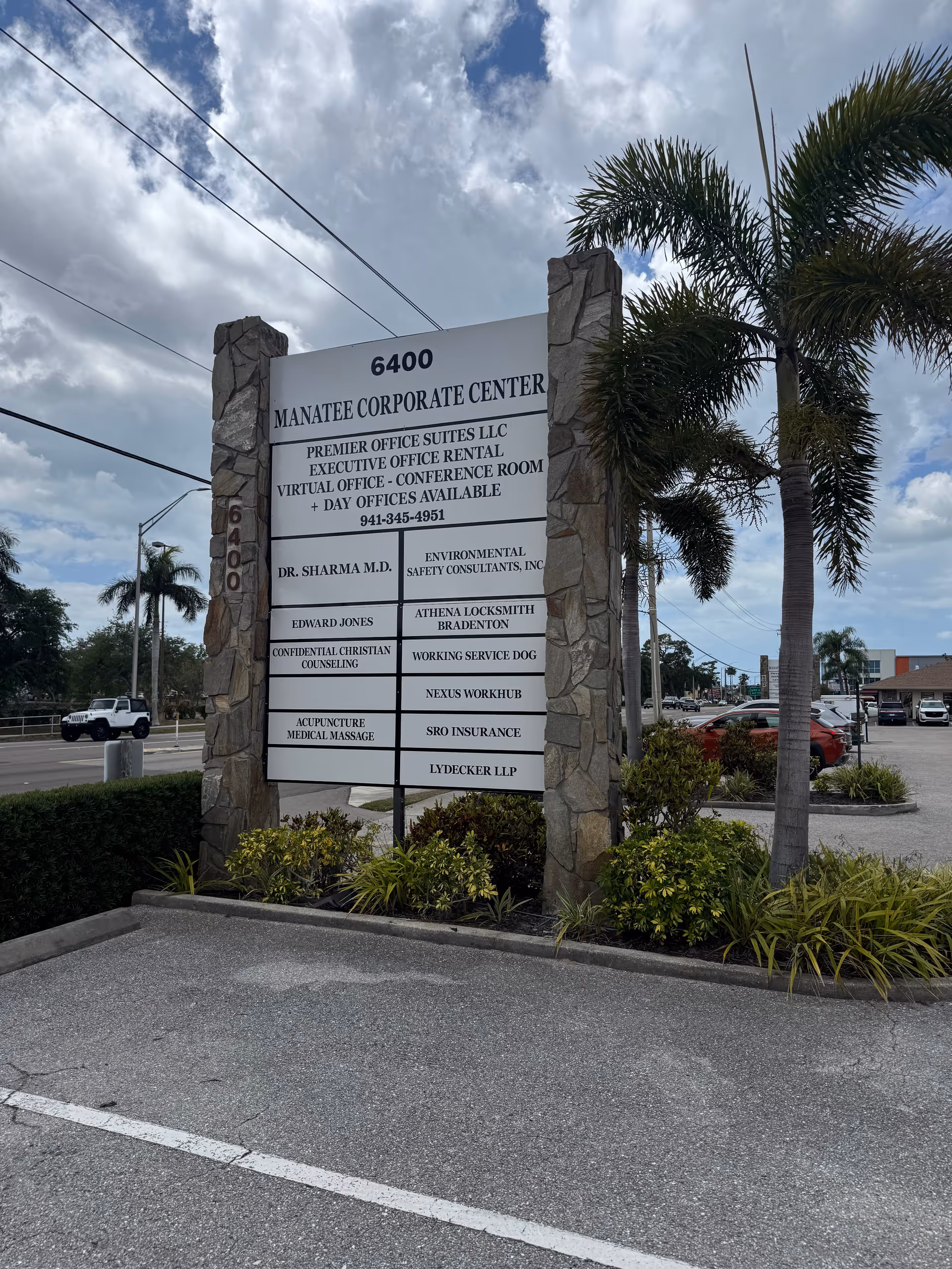 Stone sign at Manatee Corporate Center with palm trees and a parking lot.