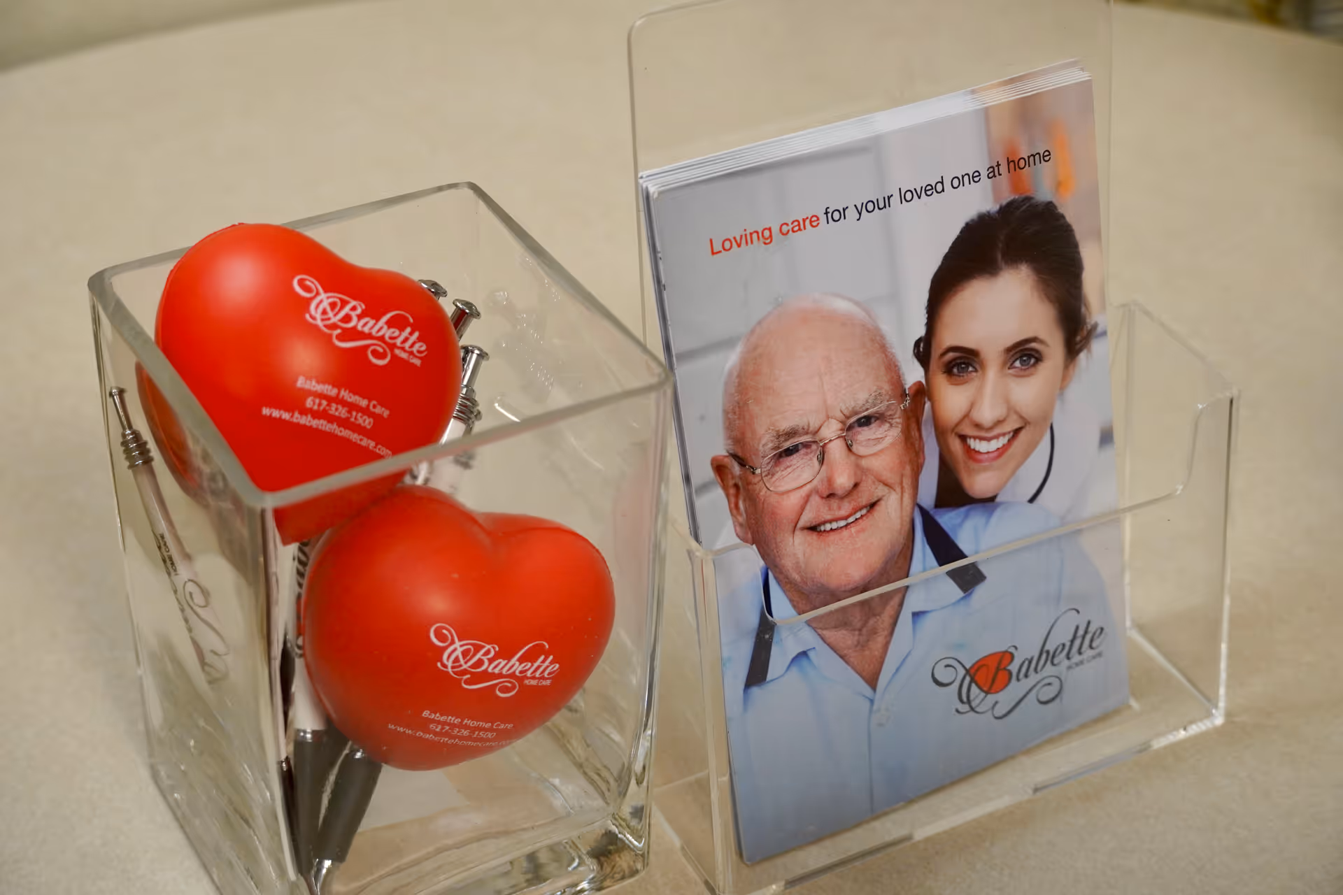 Clear acrylic desk display holding two red heart shapes and a Babette Home Care brochure