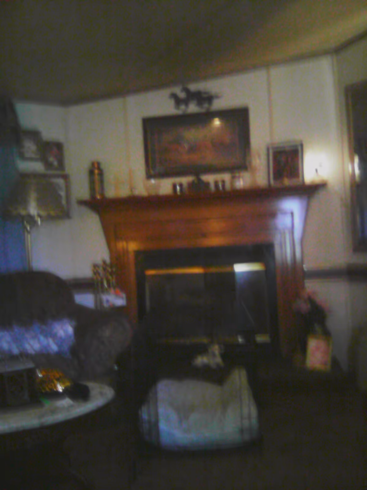Cozy living room with a wooden fireplace mantle, framed artwork, and comfortable seating.