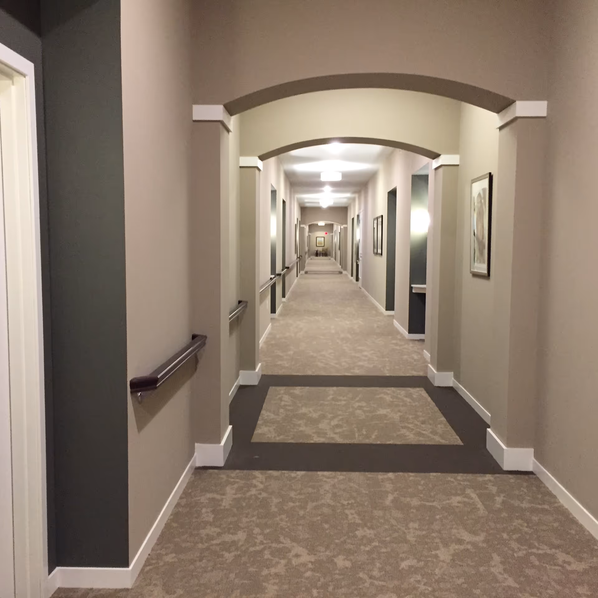 A long beige corridor with arches, carpet, and framed pictures.
