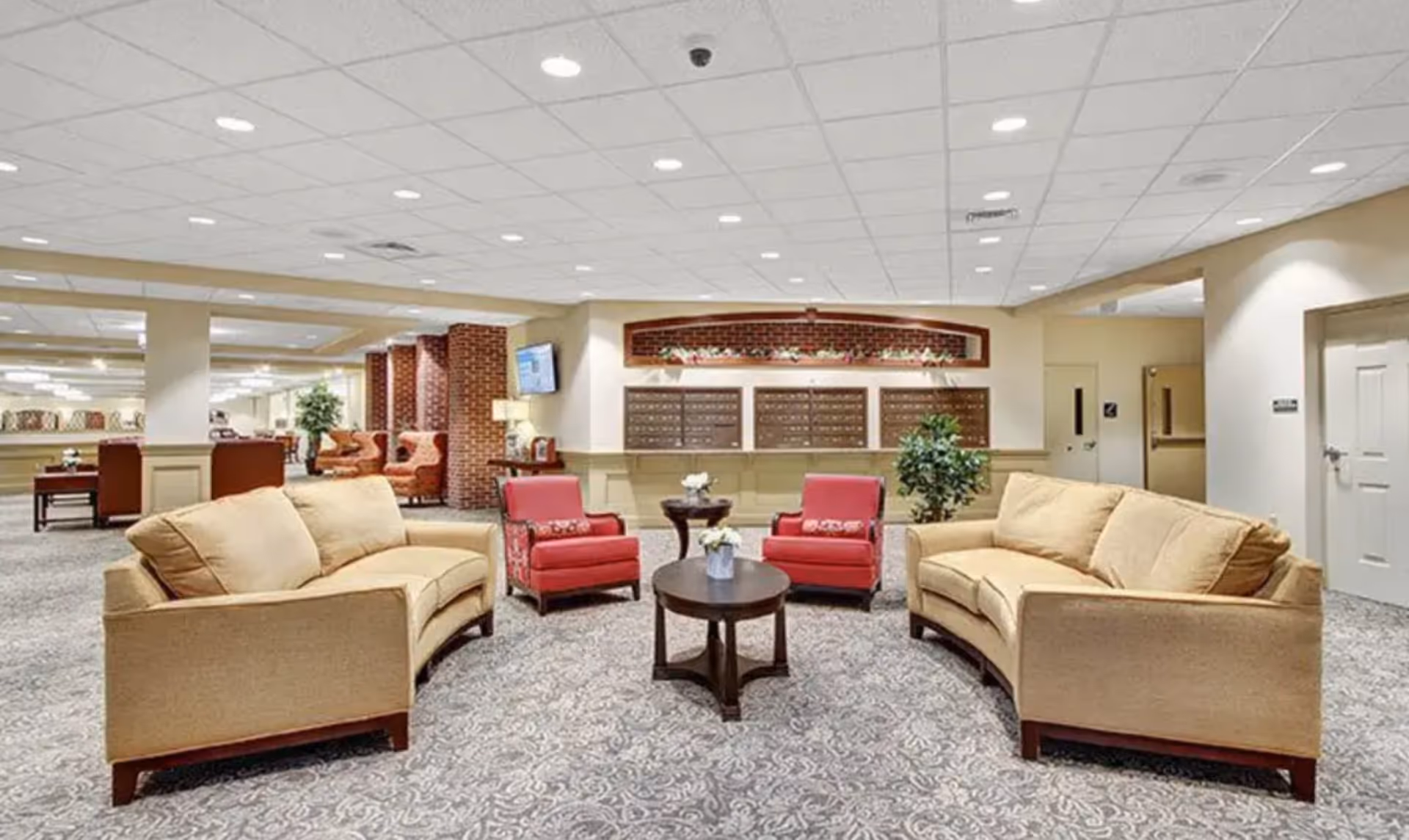 A spacious beige lounge with red chairs, beige sofas, and a round coffee table.