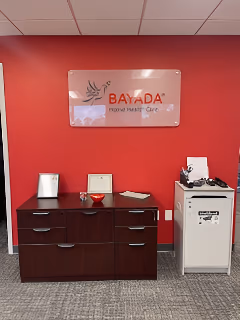 Interior office area with red wall, BAYADA sign, dark wood cabinet, and office equipment.